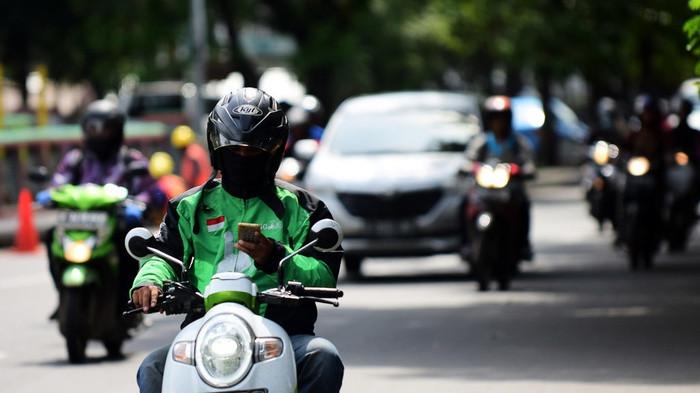 Ilustrasi pengendara ojek online mengendarai motor. (Arimacs/tirto)